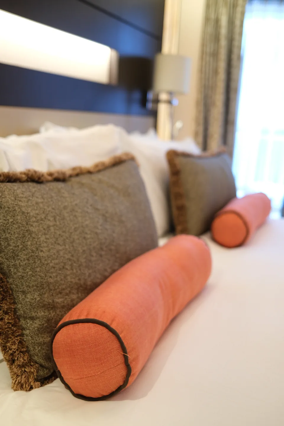 Sengen i soveværelset i Haven-suite 13906 på Norwegian Escape med grå puder og orange pøllepuder