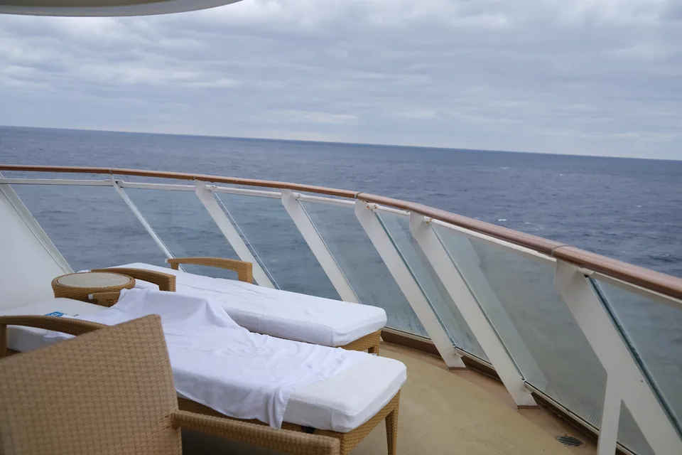 Terrassen til Haven-suite 13906 med to solstole og buet glasrækværk ud mod havet på Norwegian Escape