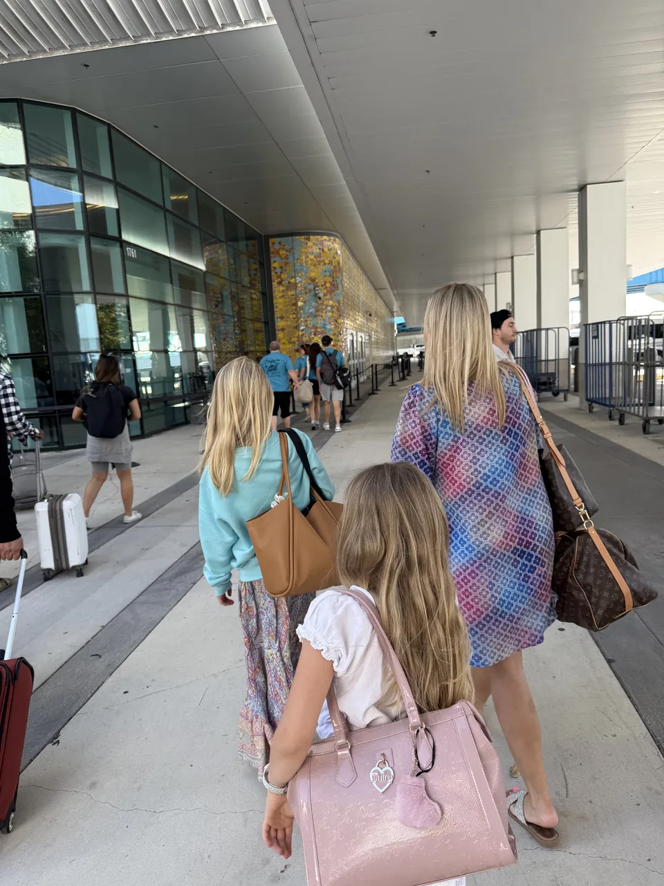 Familien på vej ind til krydstogtterminalen i PortMiami med tasker, set bagfra langs glasfacaden