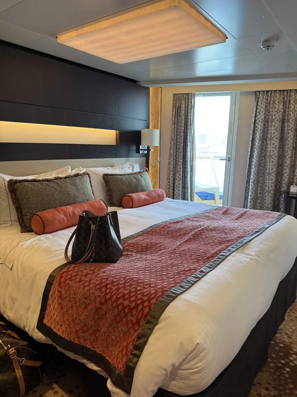 Soveværelset i Haven-suite 13906 på Norwegian Escape med dobbeltseng, rød sengeløber og dør til terrassen