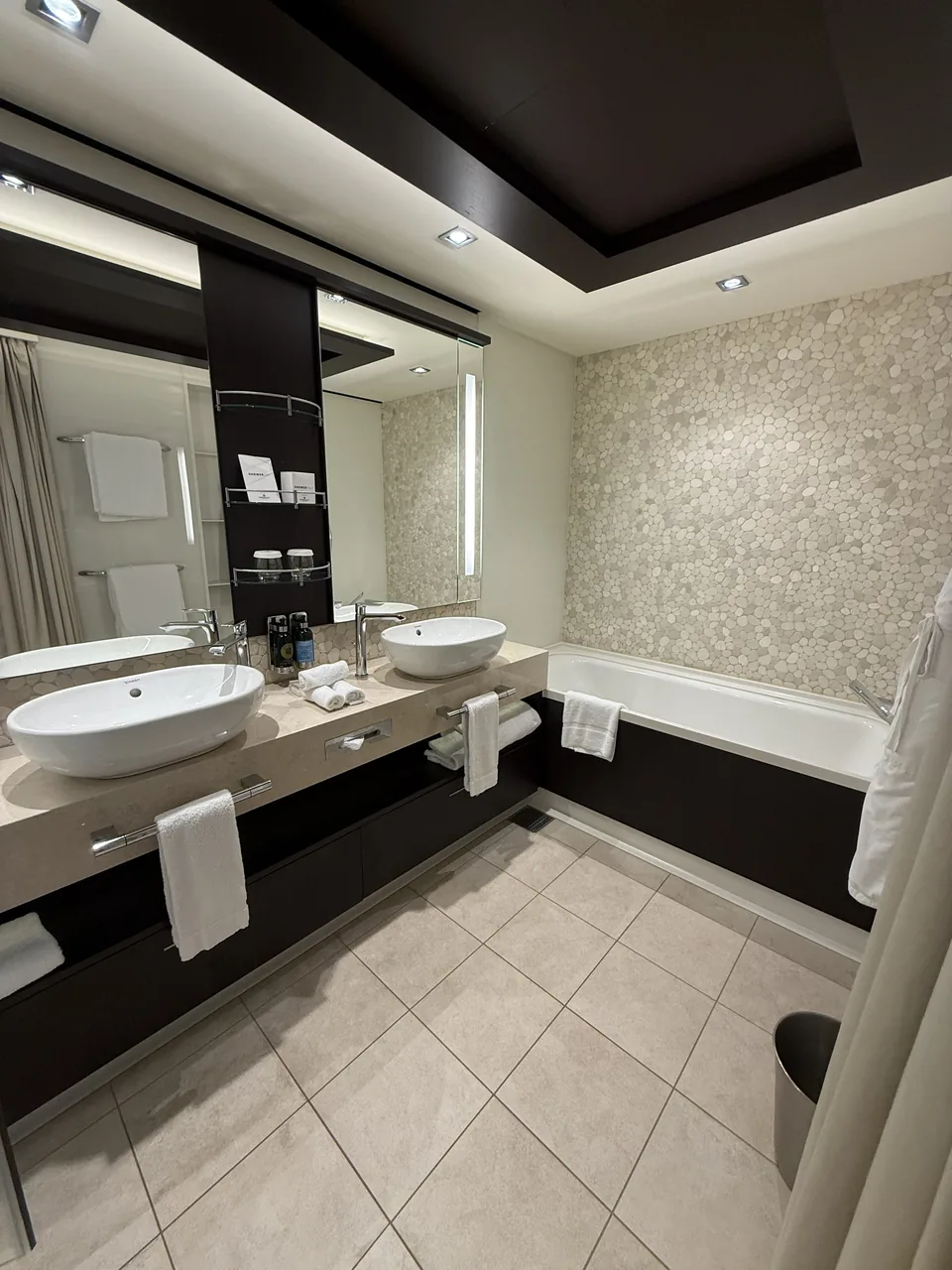 Hovedbadeværelset i Haven-suite 13906 med to håndvaske, badekar og mosaikvæg af småsten på Norwegian Escape