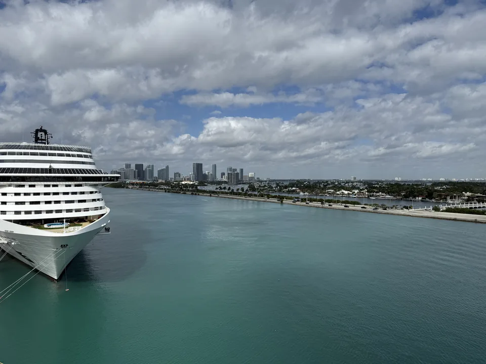 Udsigt fra Norwegian Escape over den turkise havnekanal i PortMiami med et naboskib og Miamis skyline
