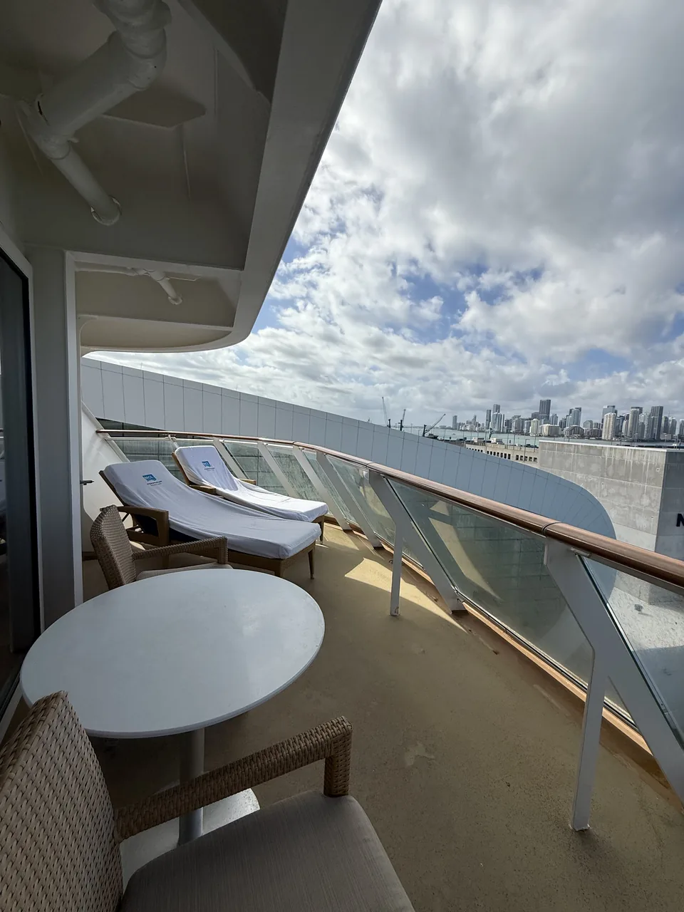 Den buede agterterrasse på Haven-suite 13906 med liggestole og Miamis skyline på Norwegian Escape