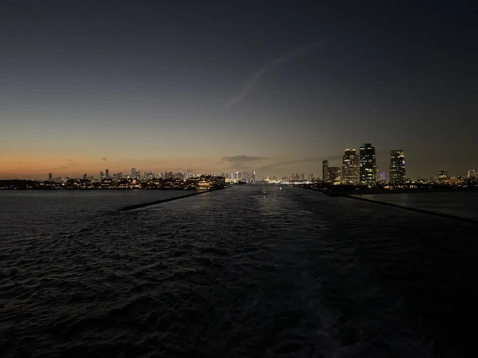 Kølvandet fra Norwegian Escape i mørket med Miamis oplyste skyline bag skibet efter afgang