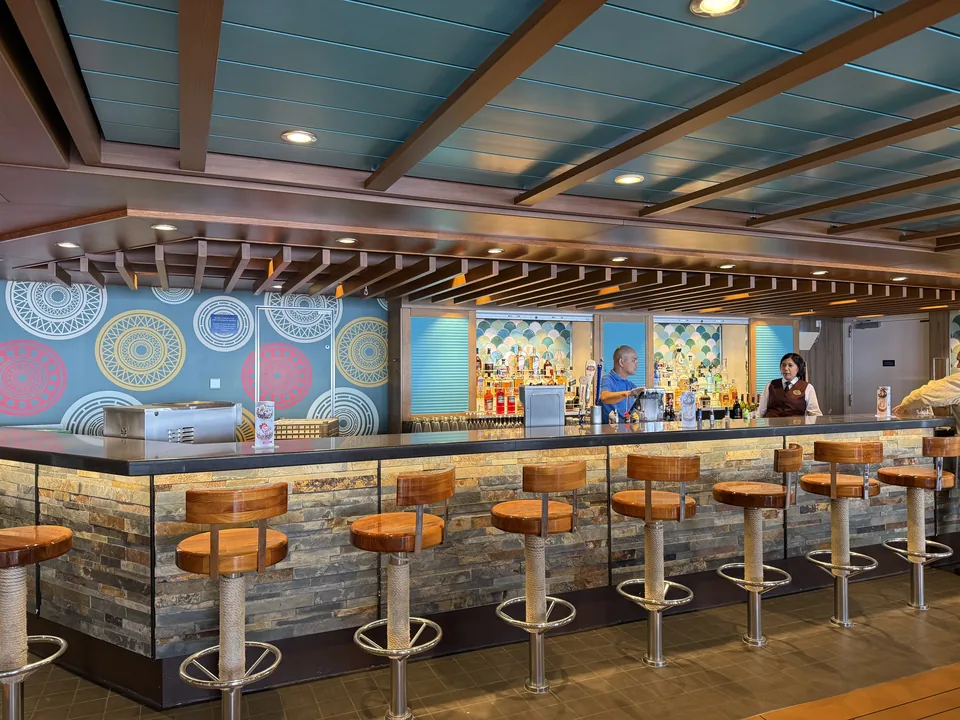 Bar med barstole i træ, stenbeklædt disk og farverig mønstervæg ombord på Norwegian Escape