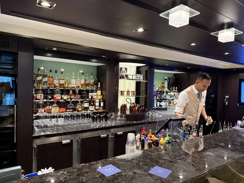 Bartender bag disken i baren i The Haven med flasker og glas på Norwegian Escape