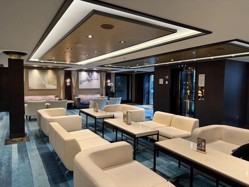 Loungen i The Haven med cremefarvede sofaer og blåt tæppe på Norwegian Escape