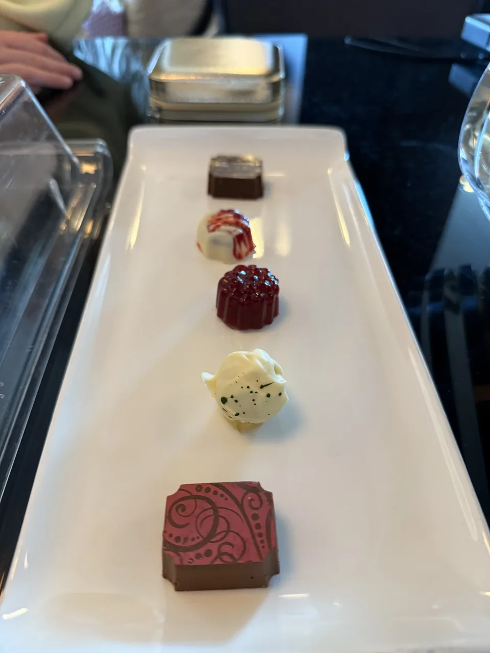 Fem praliner i forskellige farver på et aflangt hvidt fad ombord på Norwegian Escape