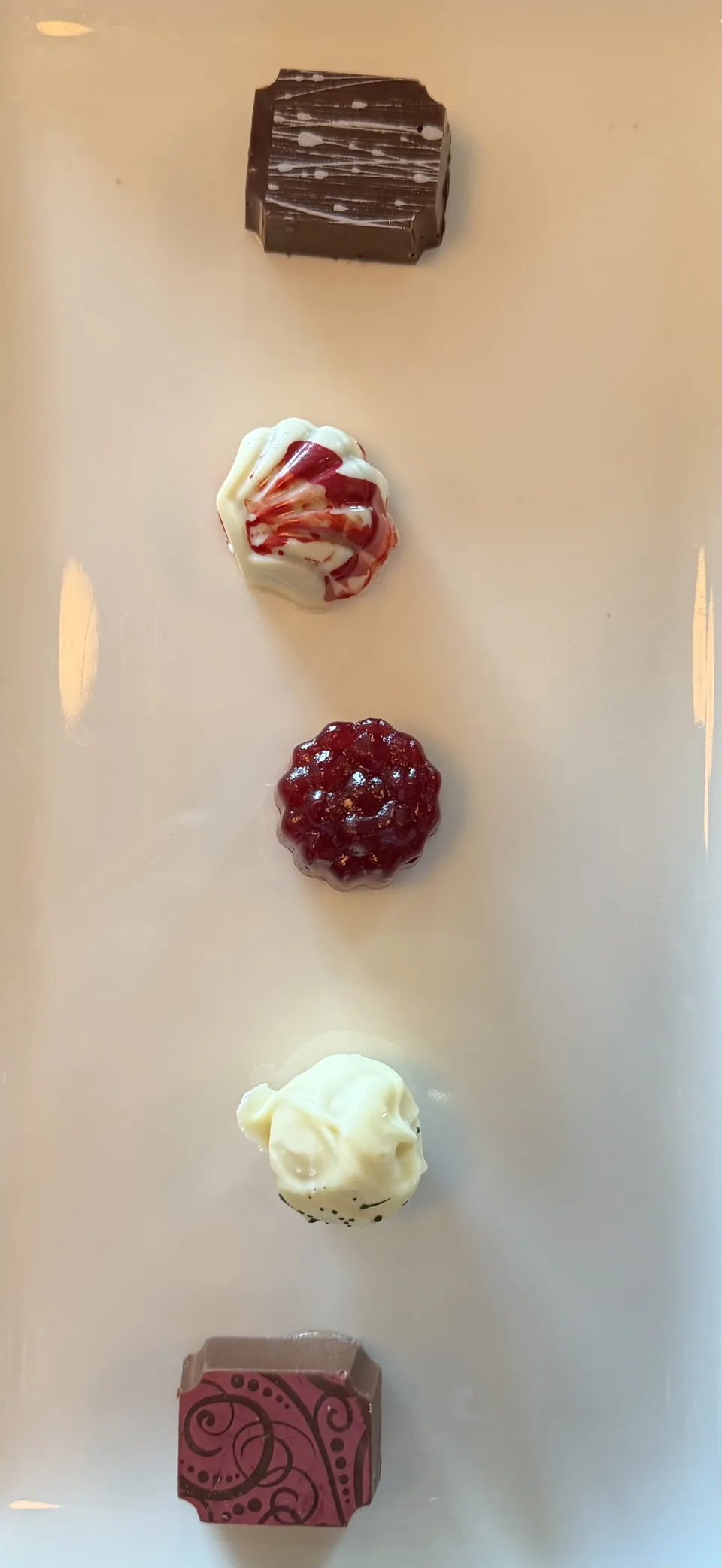 Fem praliner af mørk og hvid chokolade set ovenfra på et hvidt fad på Norwegian Escape