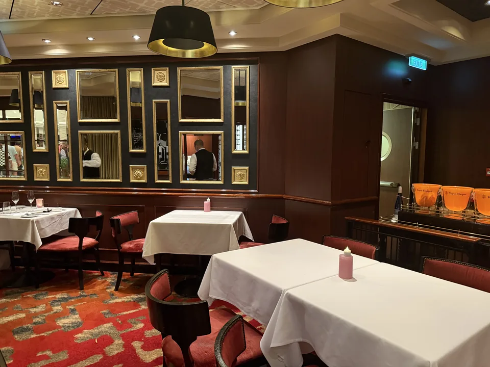 Spisesalen på Le Bistro med forgyldte spejle, hvide duge og rødt tæppe på Norwegian Escape