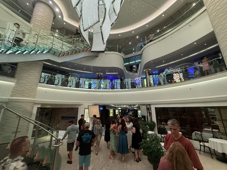 Atriet på Norwegian Escape fyldt med gæster om aftenen under den store krystallysekrone