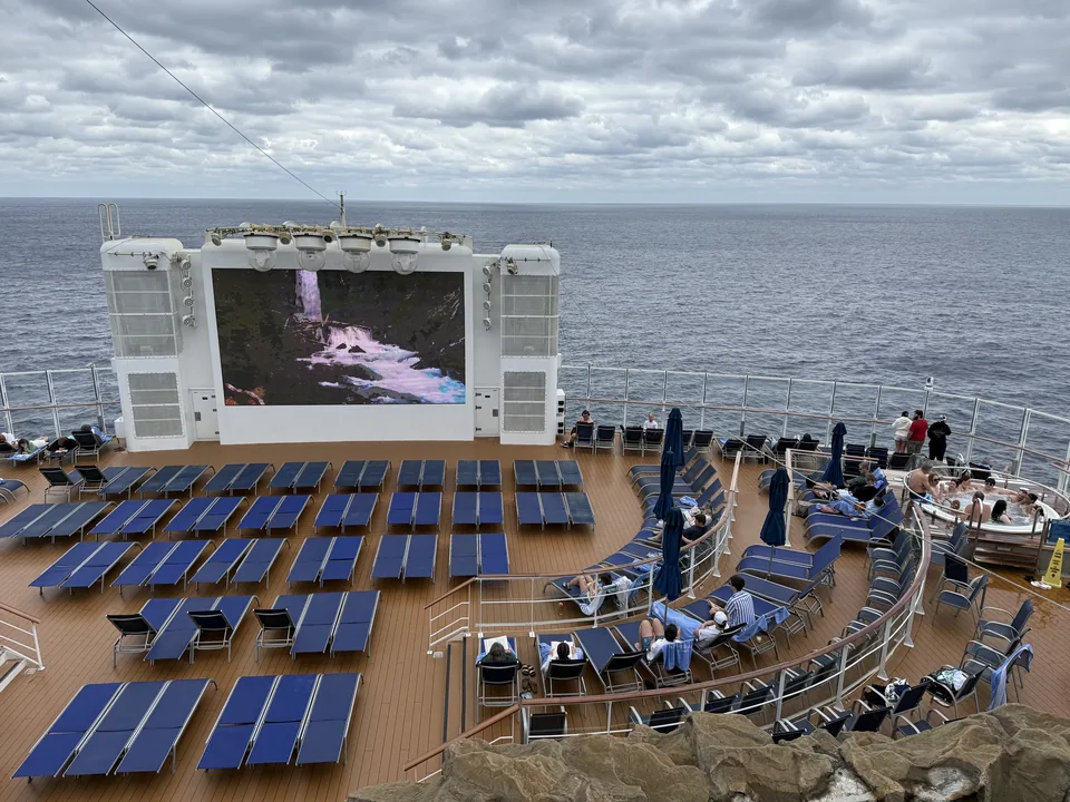 Solstole, storskærm og boblebade på agterdækket af Norwegian Escape med åbent hav på havdagen