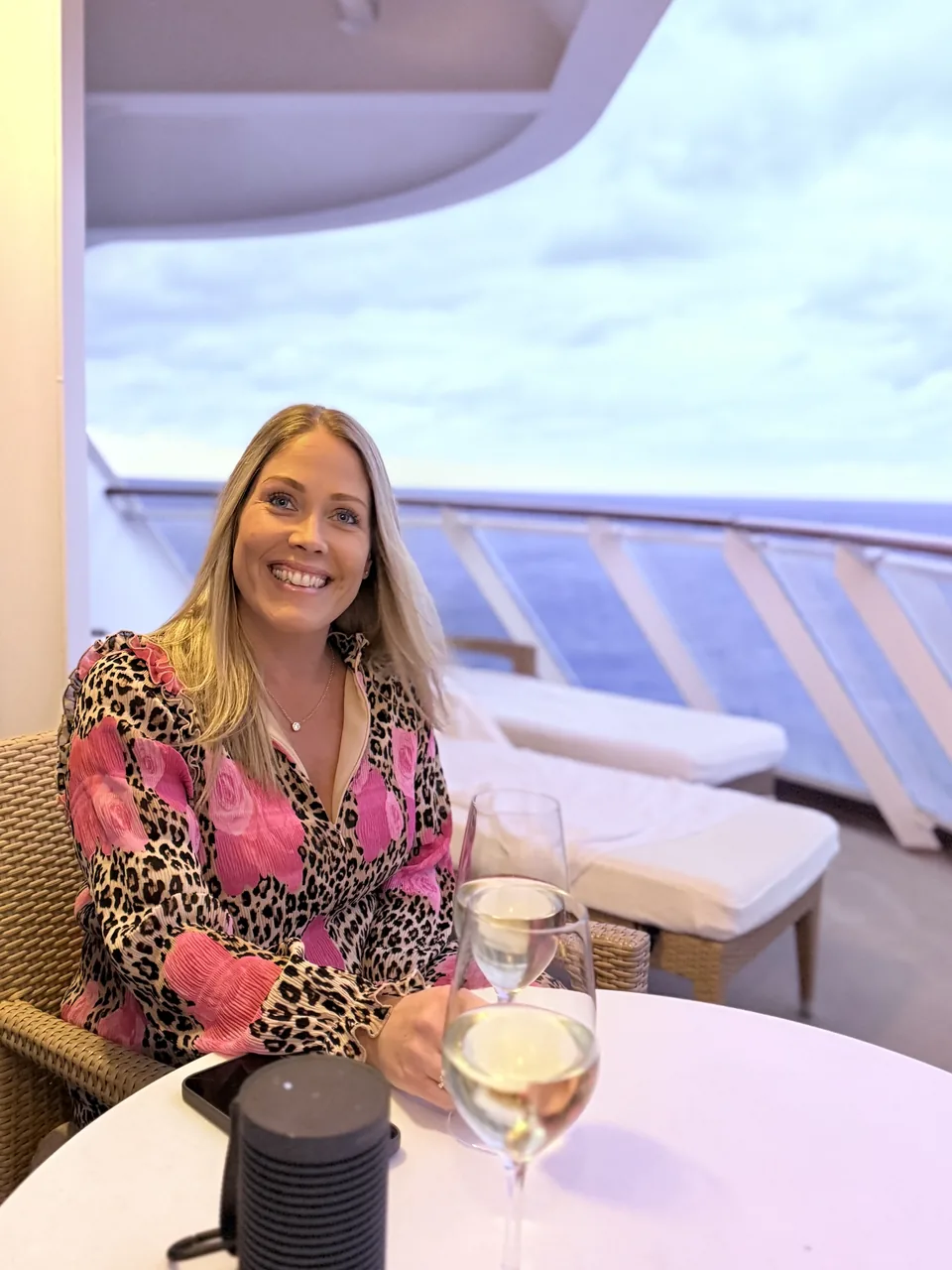Dianna med et glas hvidvin på terrassen til Haven-suiten på Norwegian Escape i skumringen