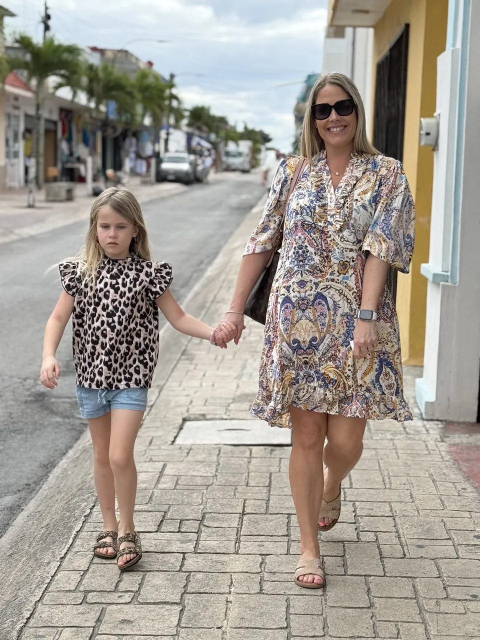 Dianna og datteren går hånd i hånd på et brostensfortov i centrum af Cozumel