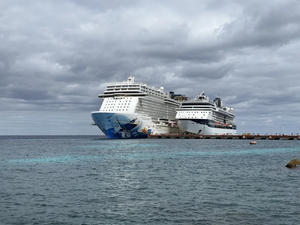 Norwegian Escape og Celebrity Constellation ved molen på Cozumel set fra land over turkist vand