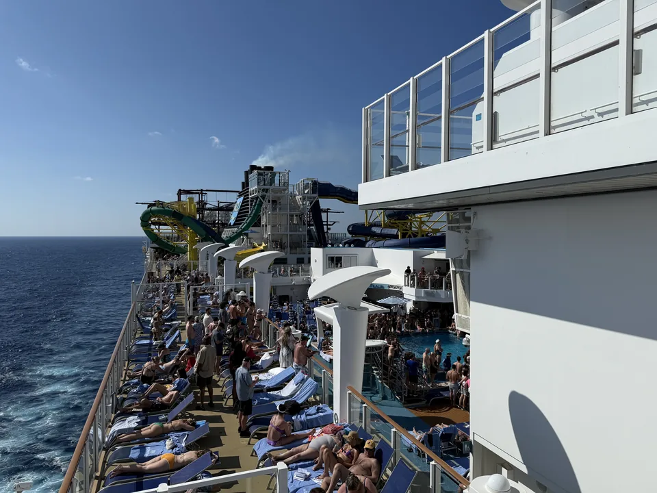 Pooldækket på Norwegian Escape med solsenge, pool og vandrutsjebaner under blå himmel på havdagen