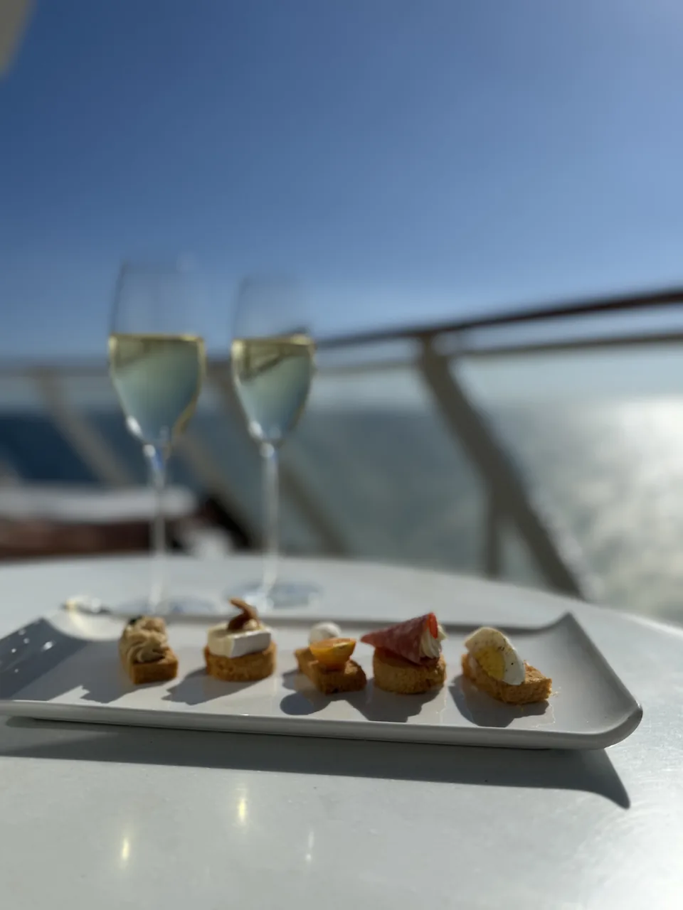 Små canapéer og to glas mousserende vin på terrassen med udsigt over havet på Norwegian Escape