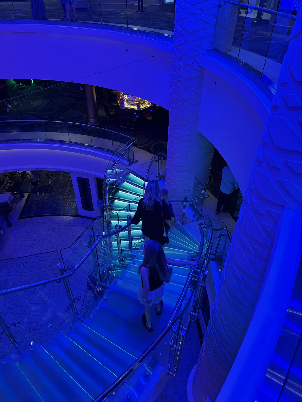 Den blåt oplyste glastrappe i atriet på Norwegian Escape om aftenen, set oppefra