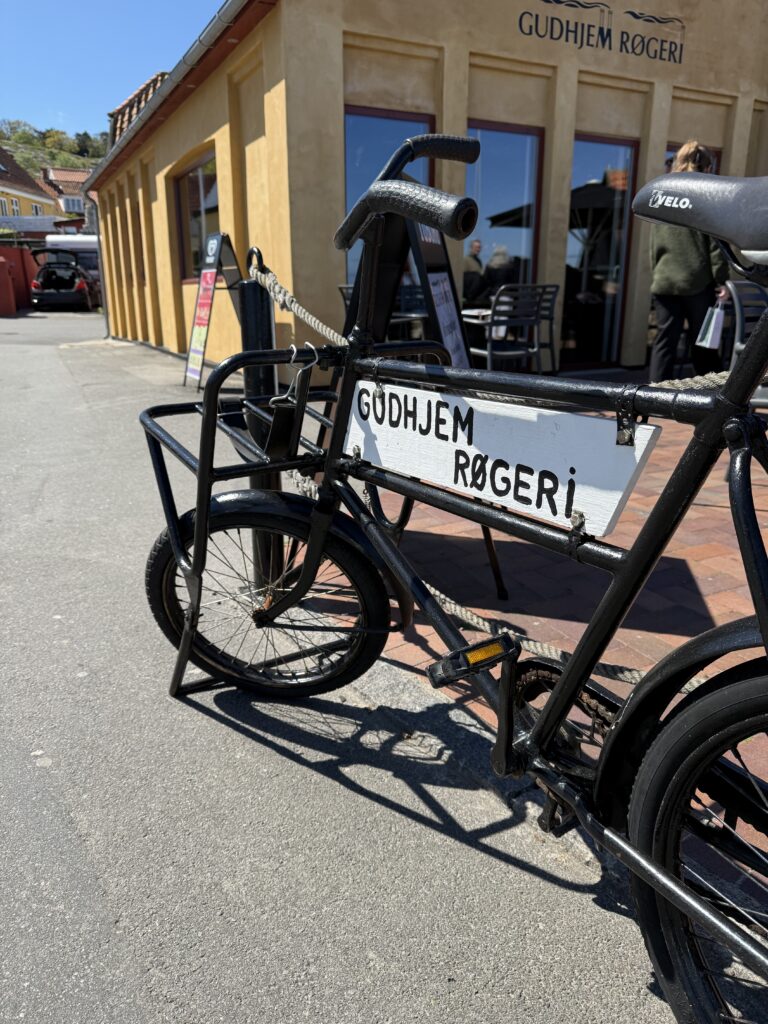 Pause med udsigt og pedaltræthed Cyklen parkeret, røgen i luften og sild på vej – Gudhjem gør det nemt at holde pitstop med stil.