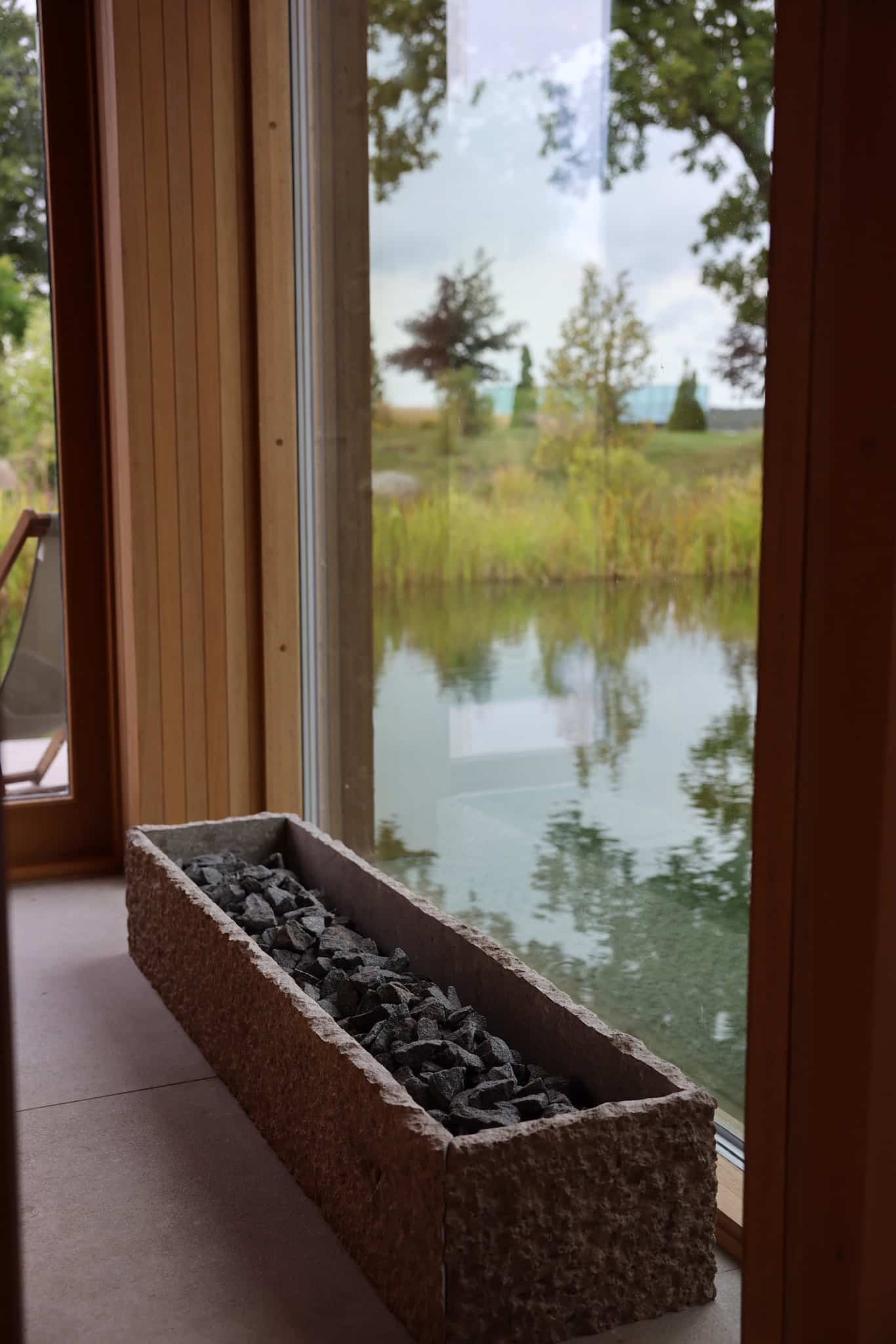 Stentrug med sten ved panoramavindue med udsigt over sø og siv