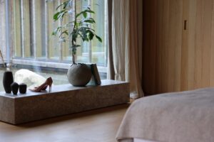Hotelværelse med stenbænk, grøn plante, stiletter og seng ved vindue