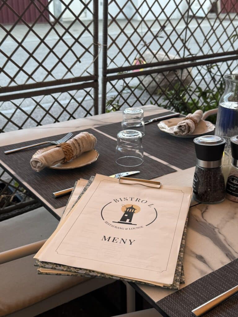 Menukort fra Bistro L på bord med servietter, glas og kværne