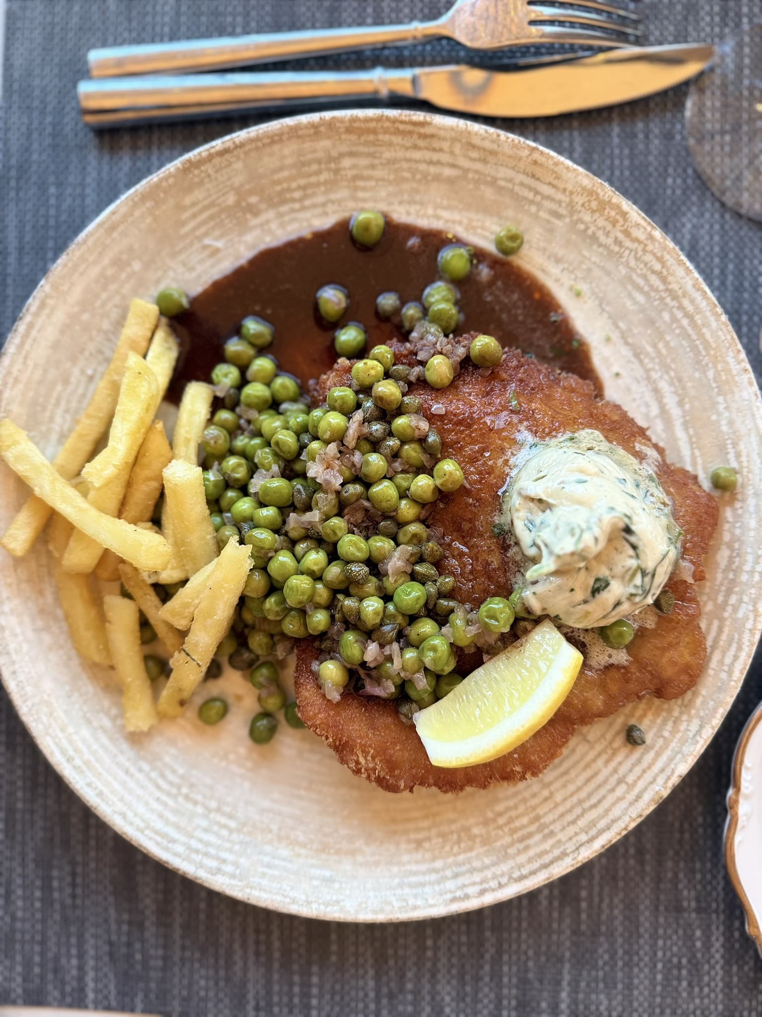Paneret schnitzel med ærter, kapers, pommes frites, citron og kryddersmør