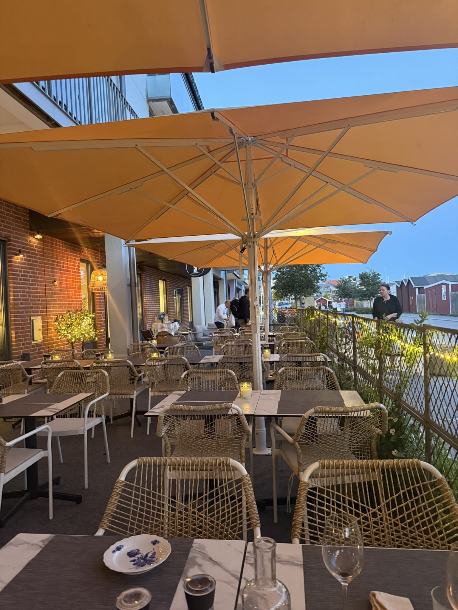 Udendørs terrasse med orange parasoller, flettede stole og borde ved havn