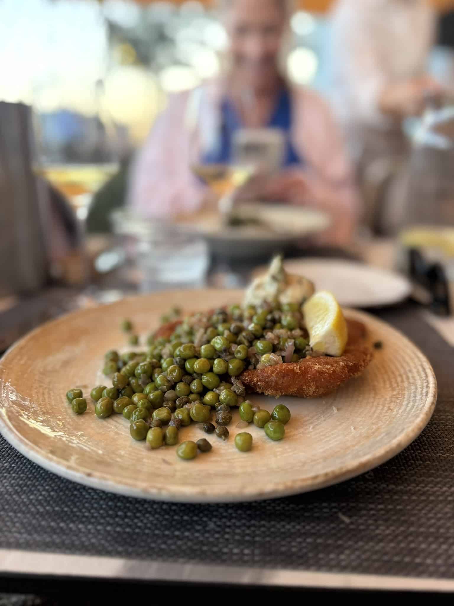 Paneret schnitzel med ærter, kapers, citronbåd og remoulade på lys tallerken
