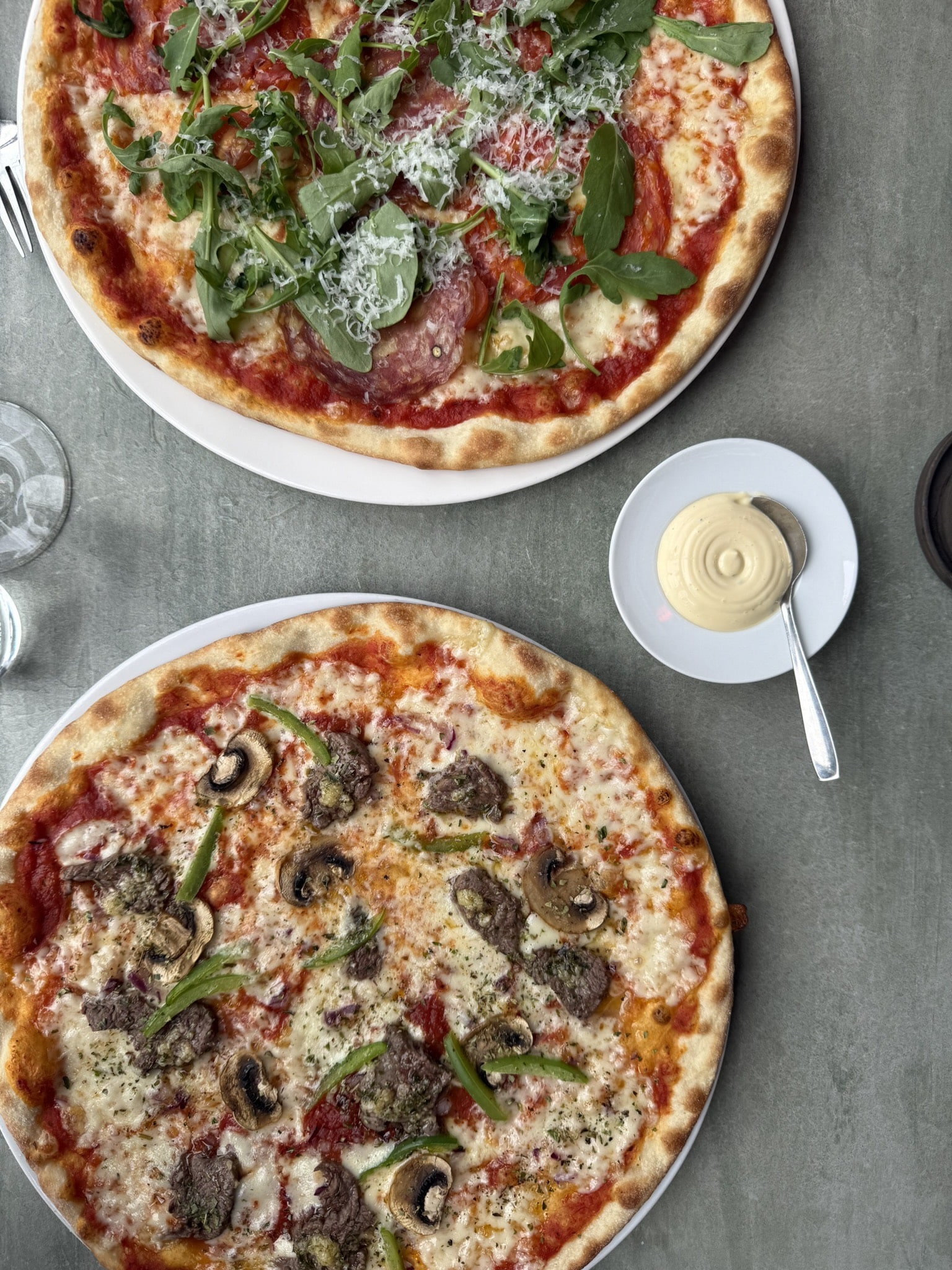 To pizzaer på hvide tallerkener med lille skål creme og ske