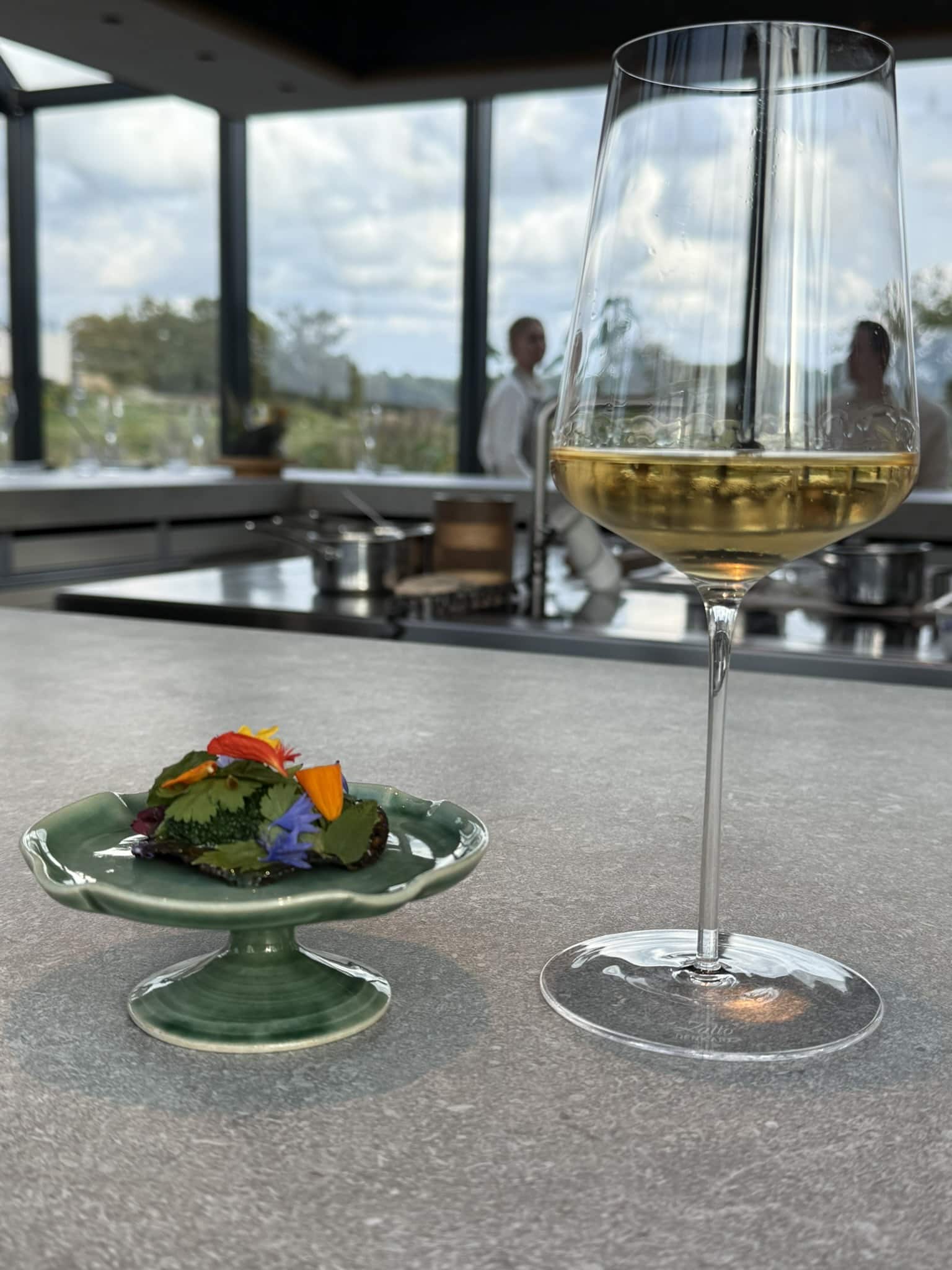 Grøn lille kagestand med blade og spiselige blomster ved glas hvidvin