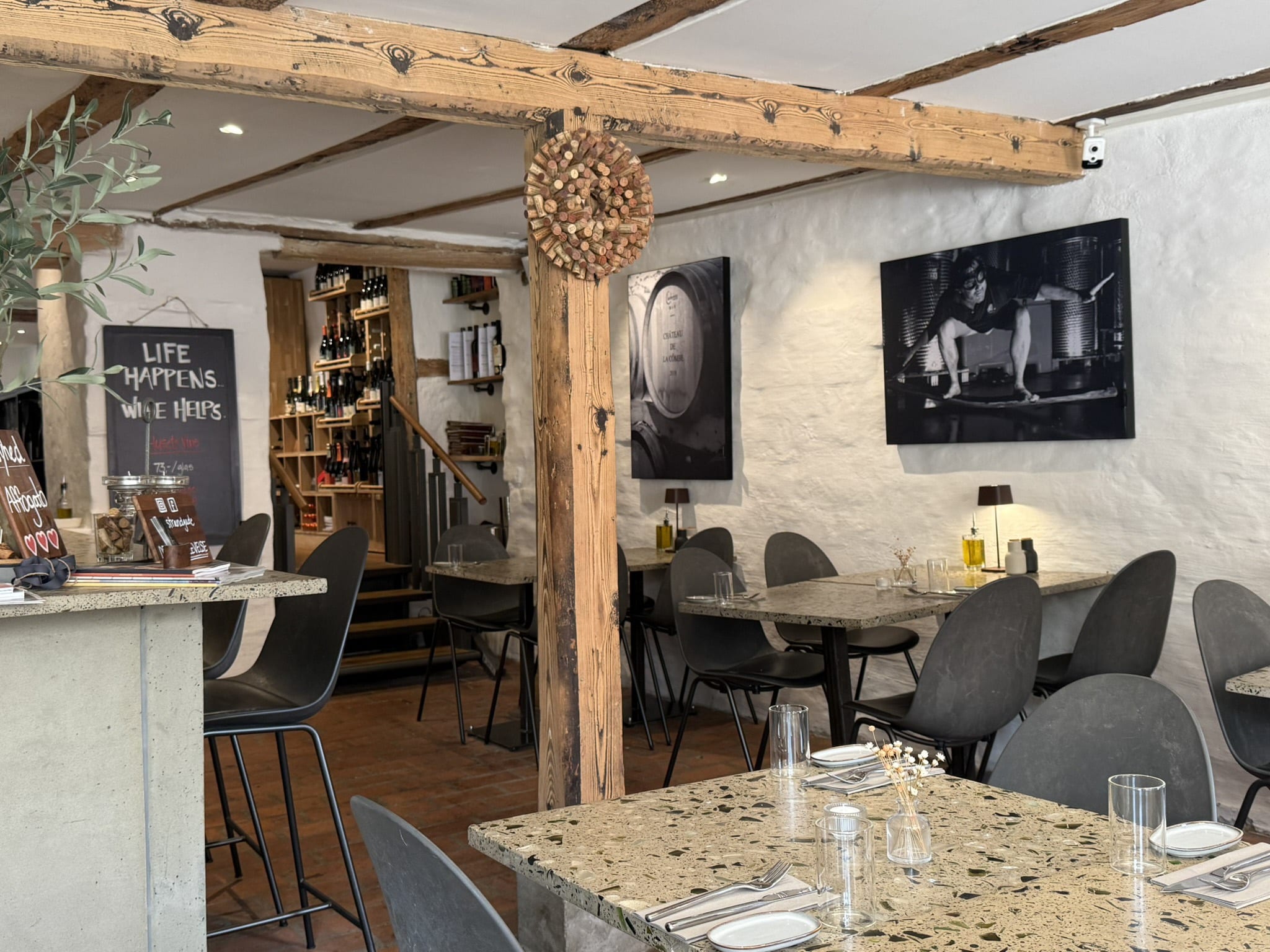 Restaurantlokale med terrazzoborde, sorte stole, træbjælker og vinreoler i baggrunden