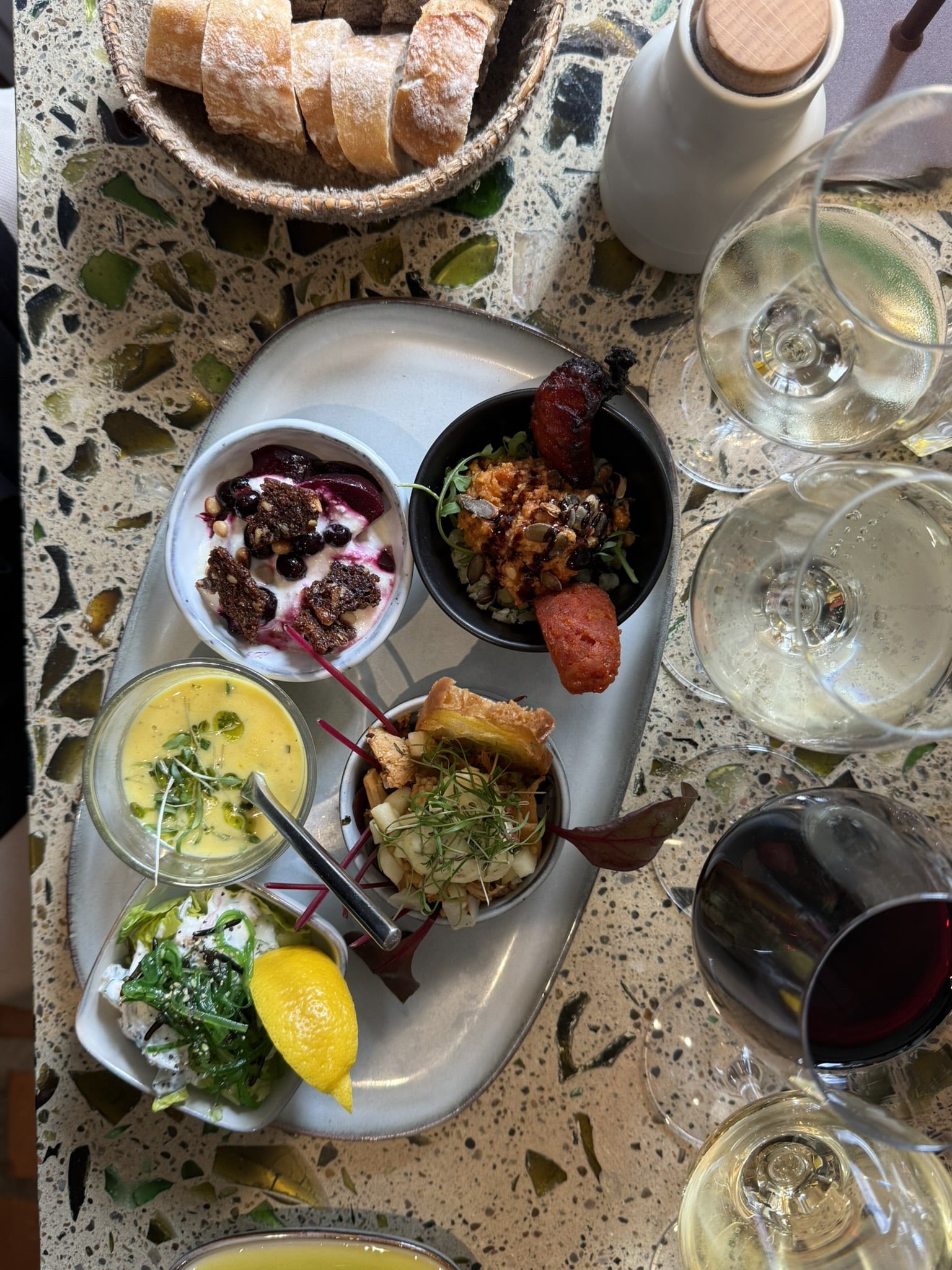Tapasbræt med fem små skåle, brødkurv og vinglas set fra oven