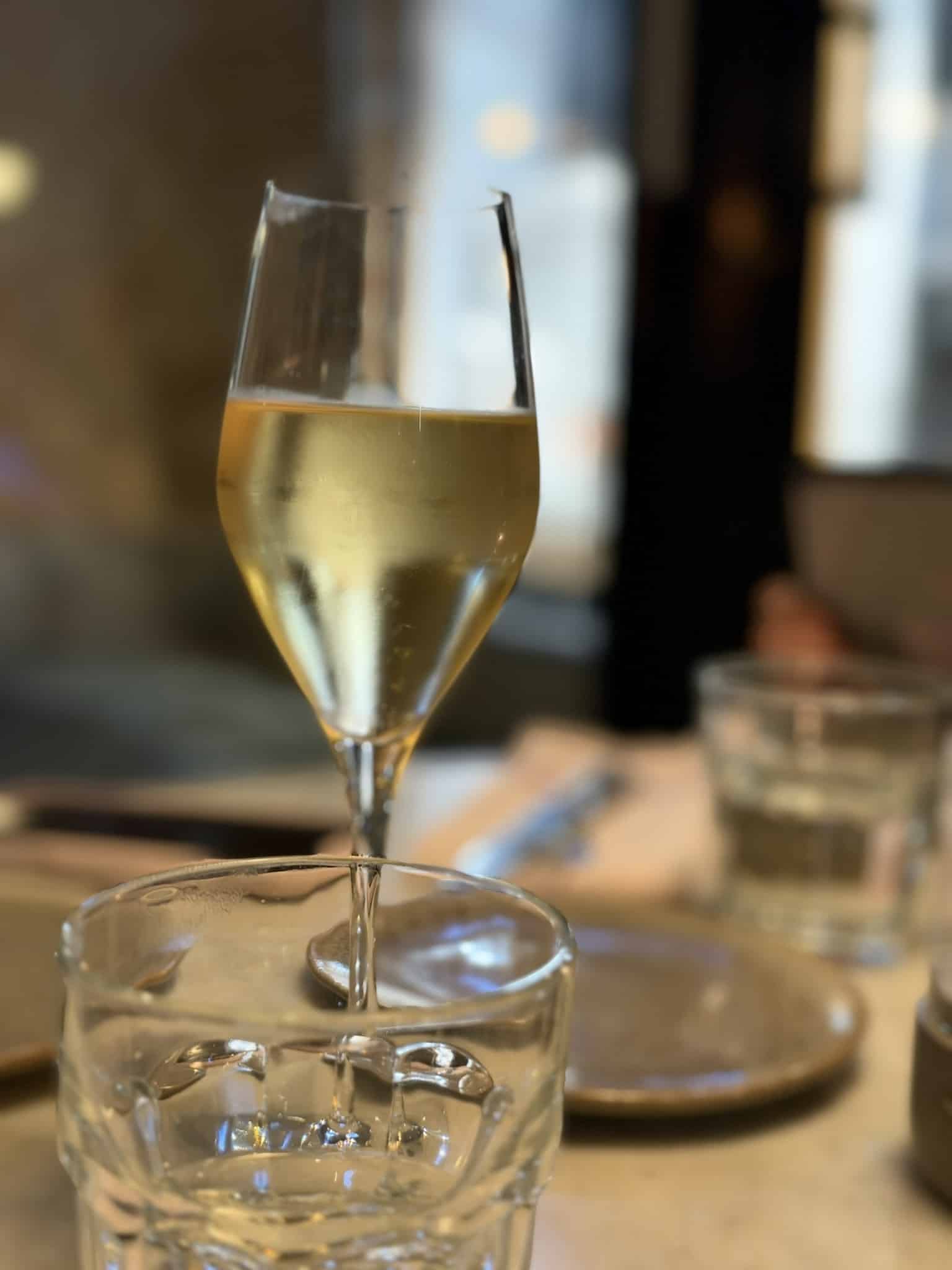Glas med lys mousserende vin foran vandglas på bord
