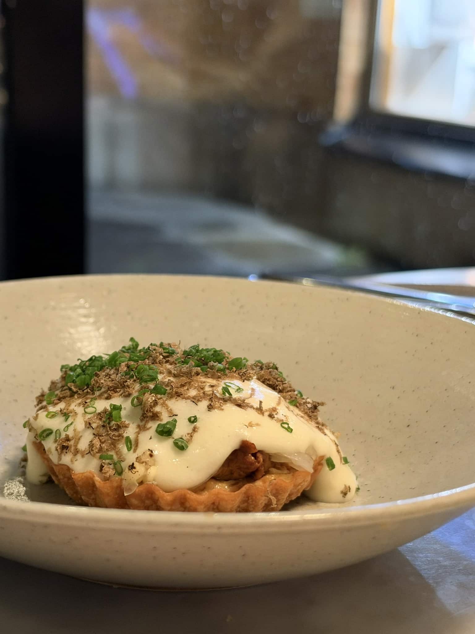 Tærte dækket af hvid creme, revet trøffel og purløg i skål