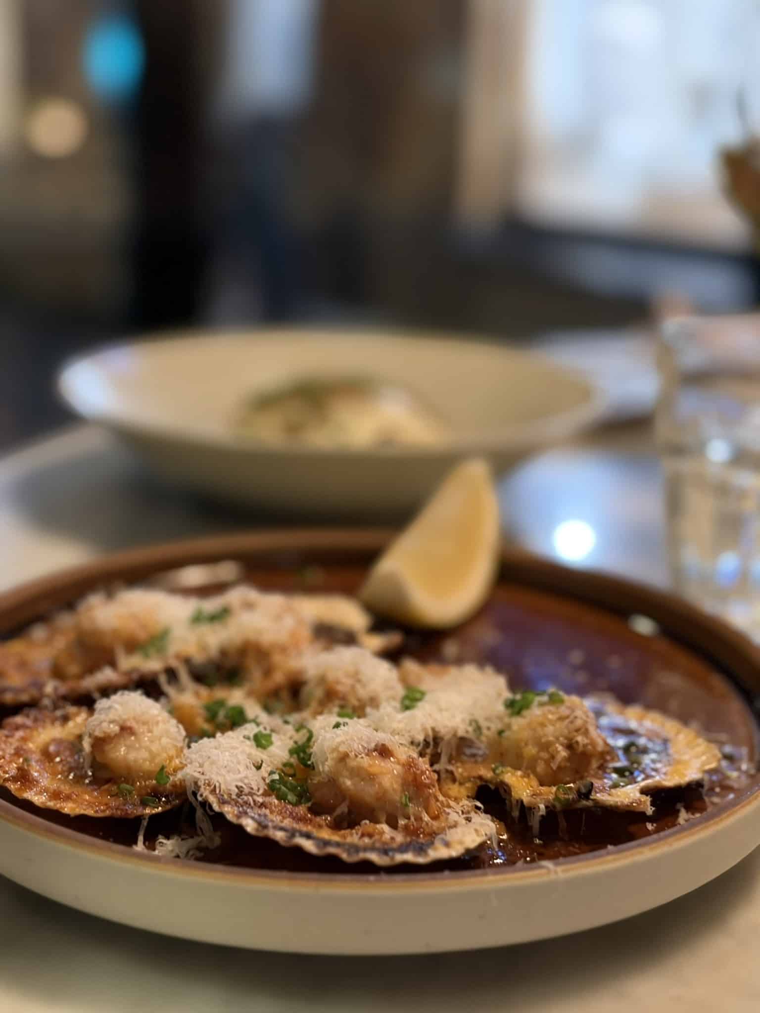 Gratinerede kammuslinger i skal med revet ost, purløg og citronbåd