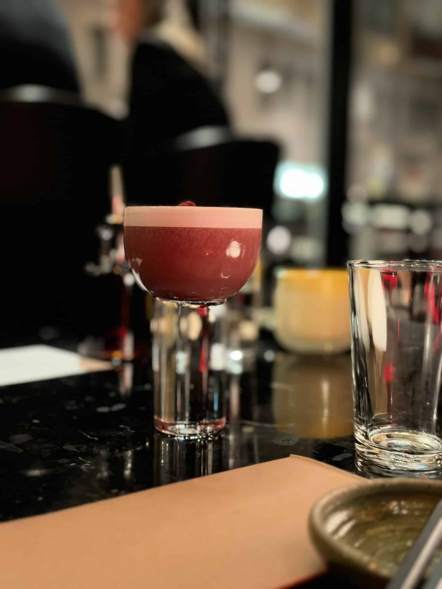Rød cocktail med skumtop i coupeglas på sort marmorbar.