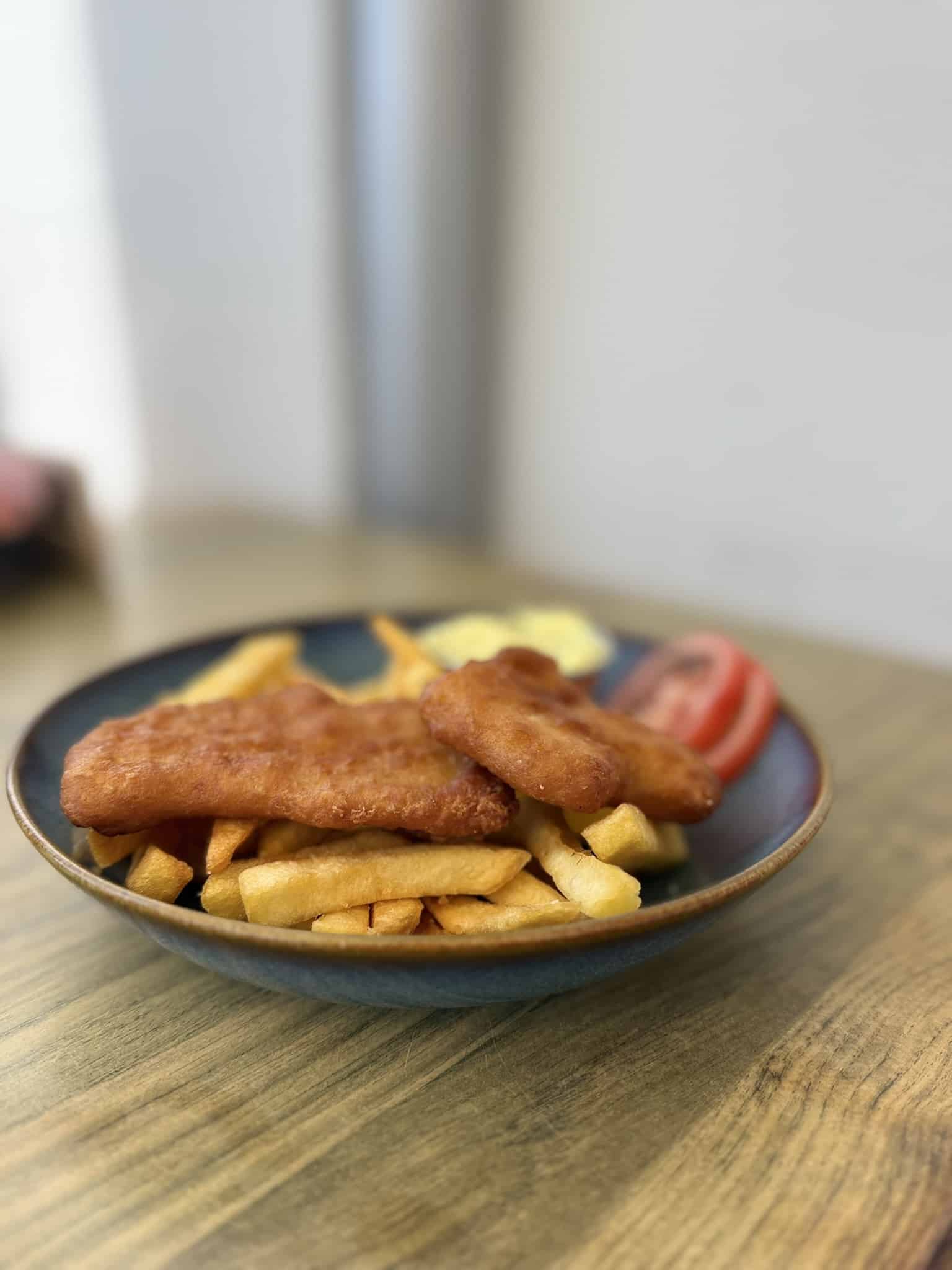 Fish and chips med to stykker paneret fisk, pommes frites, remoulade og tomat