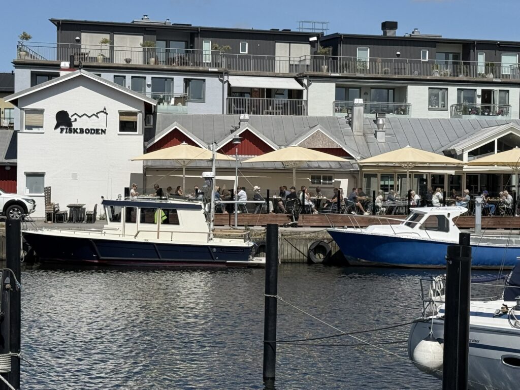 Fiskboden set fra havnen med både, parasoller og gæster på terrassen