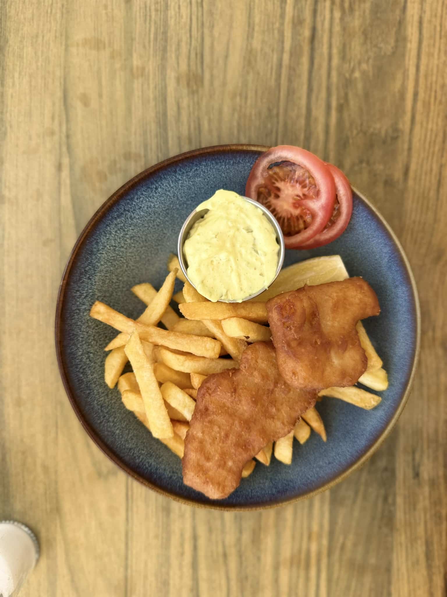 Fish and chips set ovenfra med remoulade i skål, tomatskiver og citron