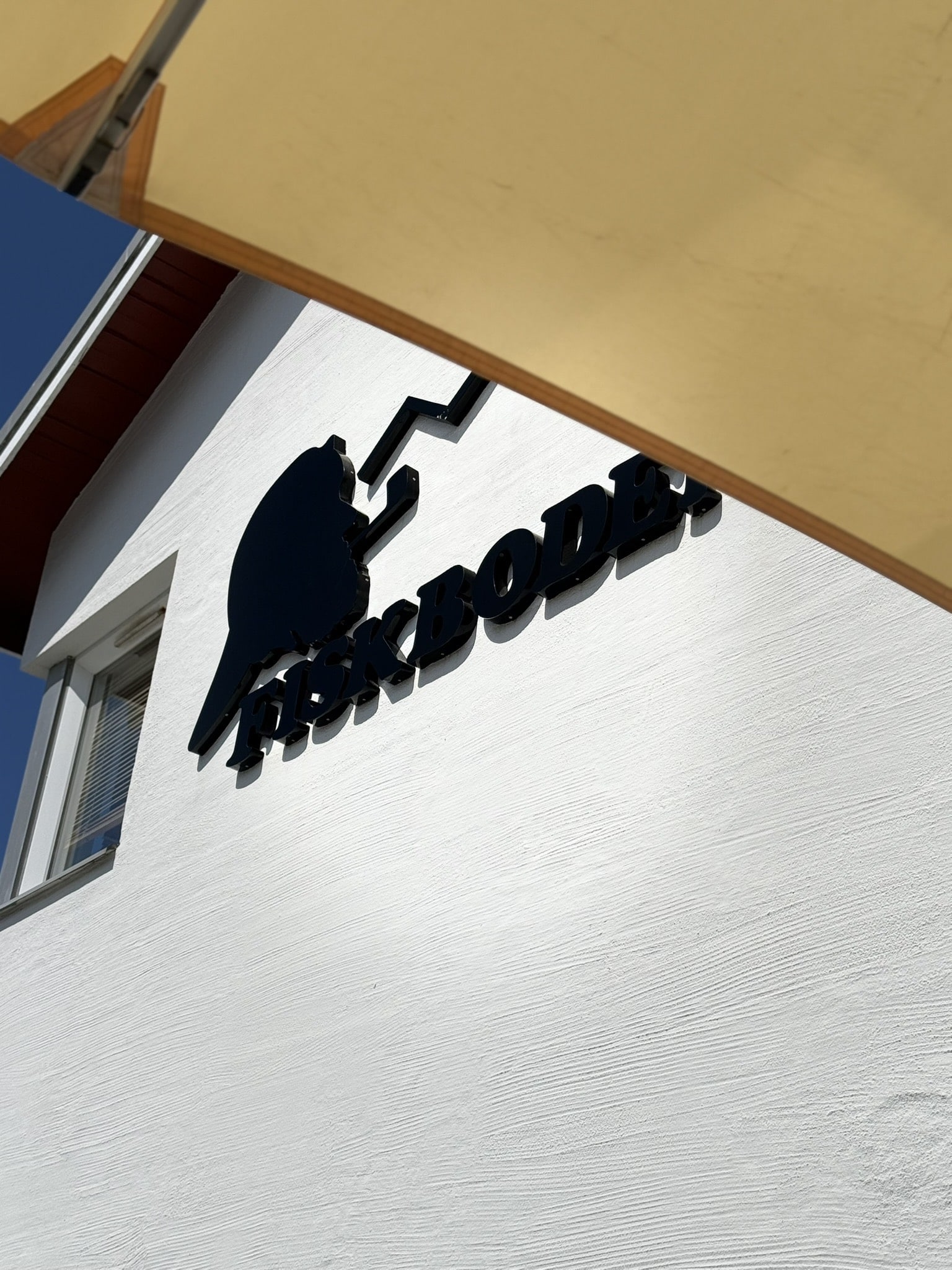 Fiskbodens sorte logo med fisk på hvid facade under gul parasol