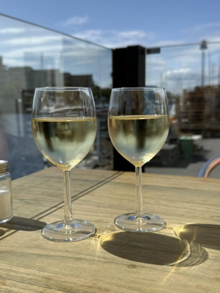 To glas hvidvin på træbord med havn og både bag glasværn