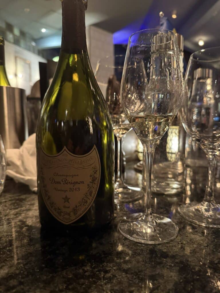 Flaske Dom Pérignon Vintage 2013 ved siden af fyldt champagneglas på bardisk.