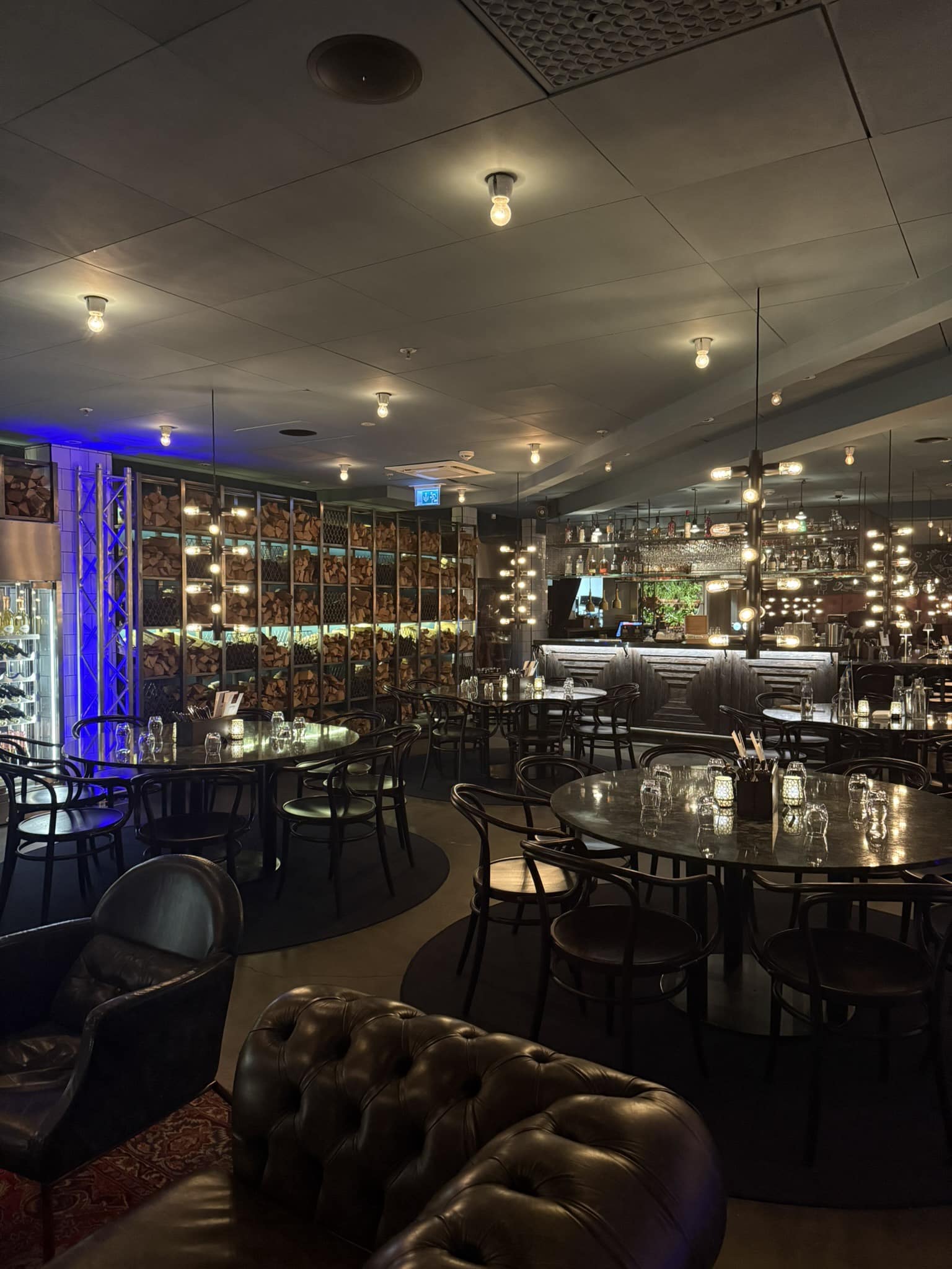Restaurantlokale med runde borde, brændestabler på væg og bar