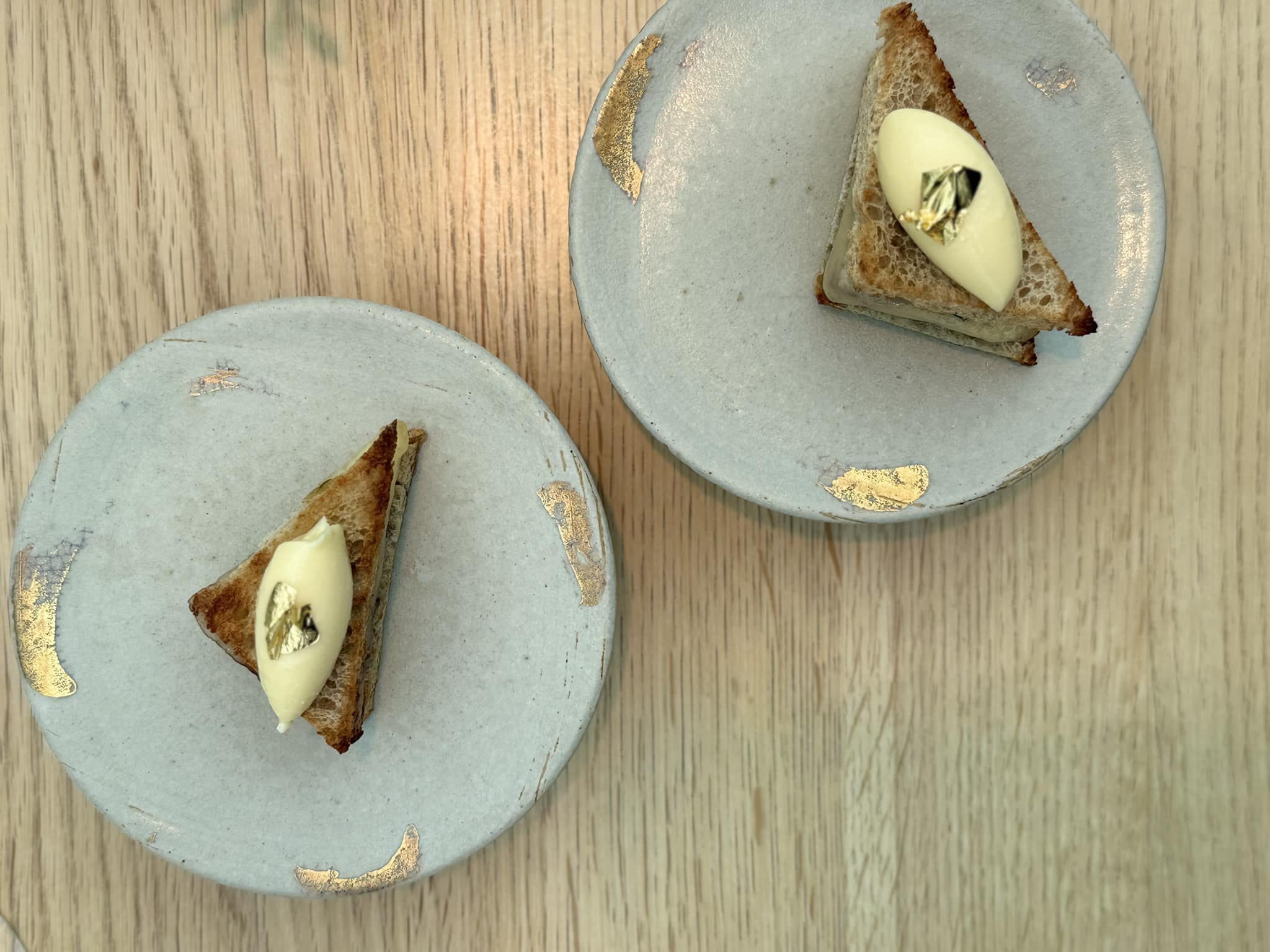 To trekantede brødstykker med creme og bladguld set ovenfra