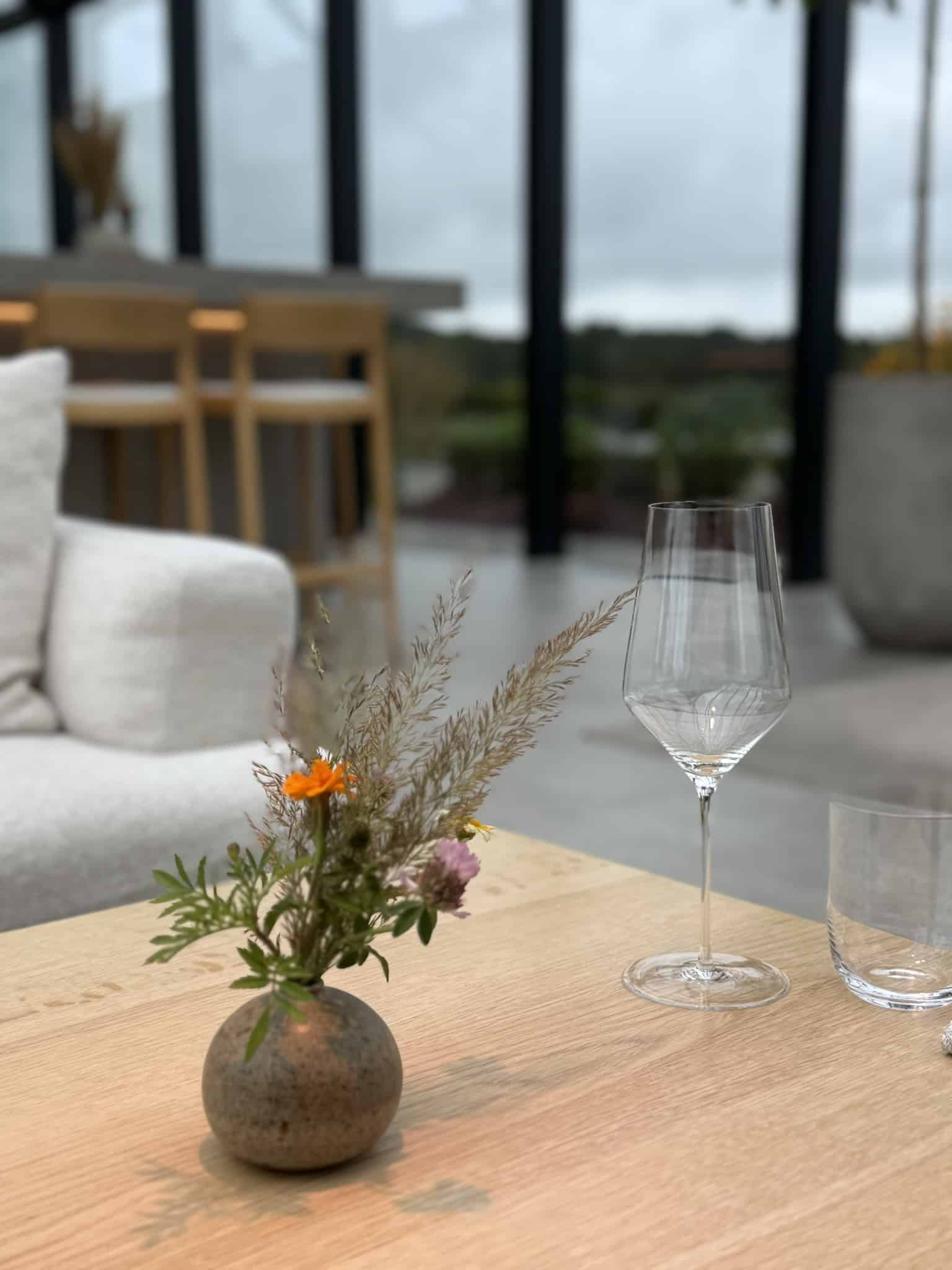 Lille vase med markblomster og tomt vinglas på egetræsbord