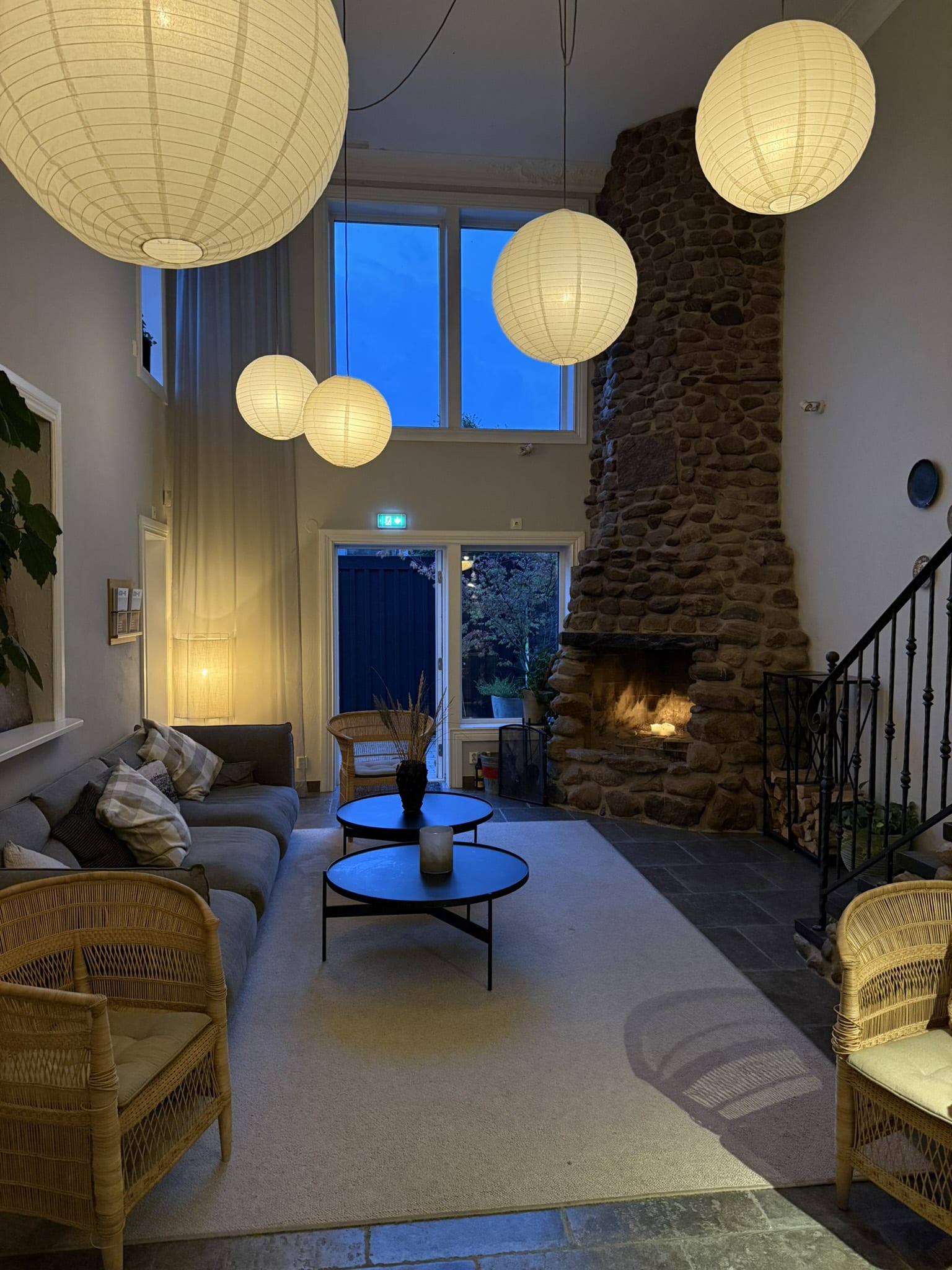 Lounge med stenpejs, grå sofa, rispapirlamper og kurvestole