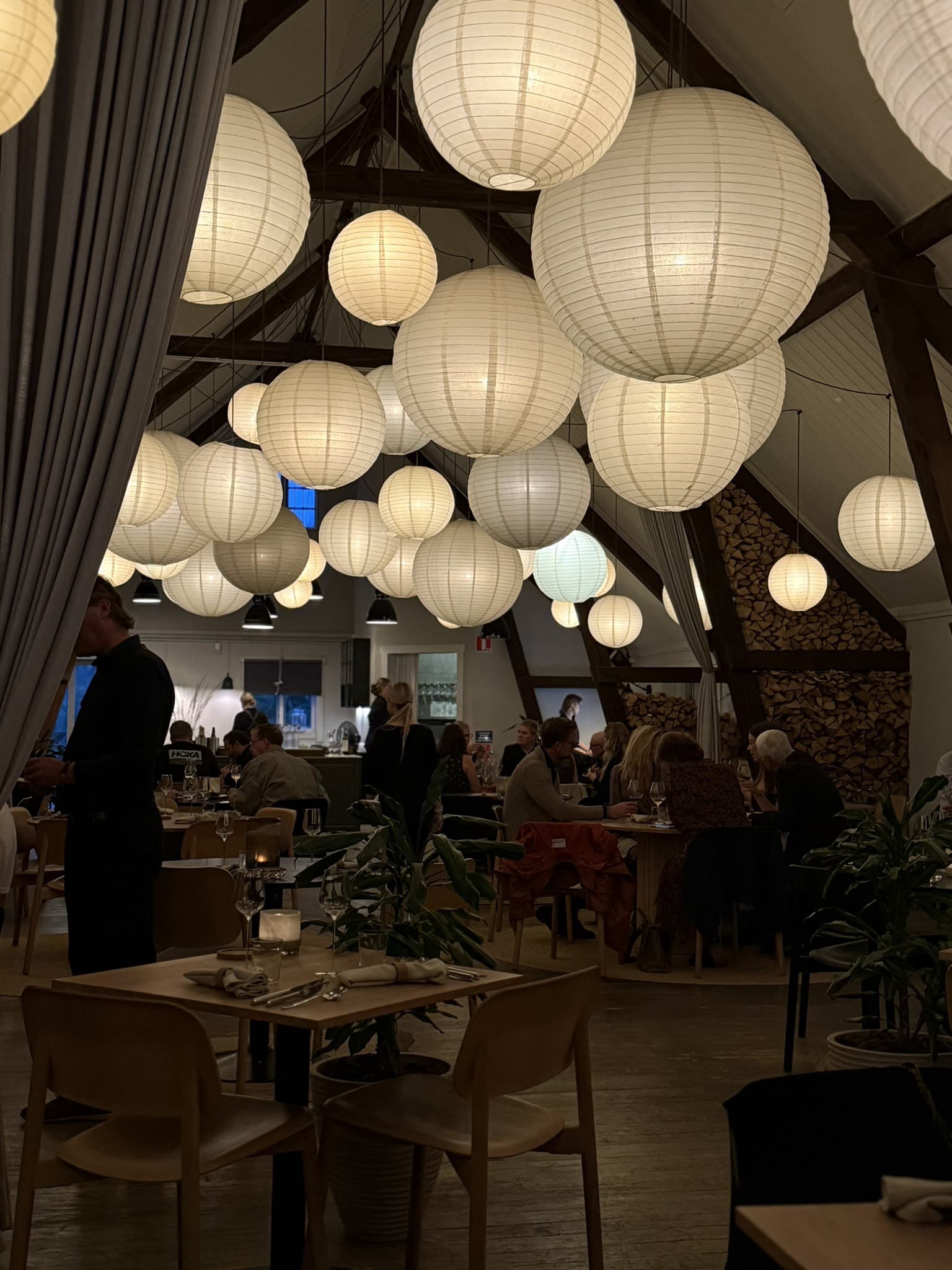 Restaurantlokale med mange rispapirlamper, træborde og spisende gæster