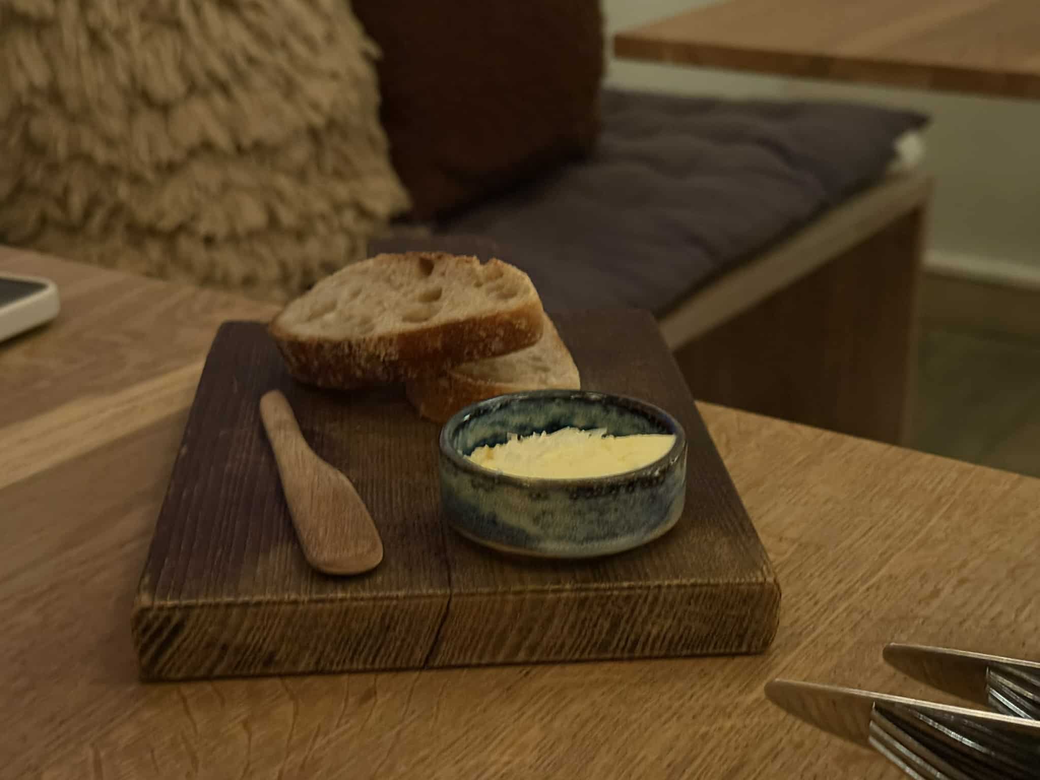 To skiver surdejsbrød med smør i keramikskål på træbræt