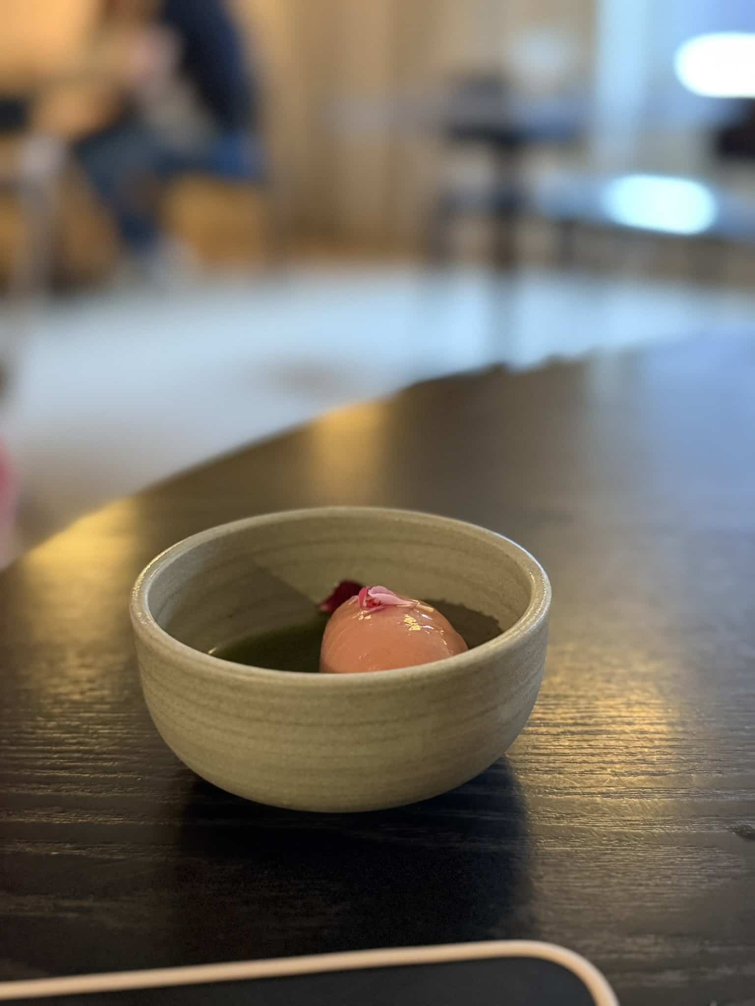 Lyserød sorbet i grøn olie med blomsterblade i keramikskål på mørkt bord